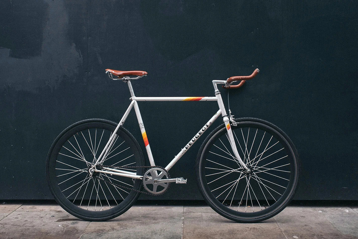  white bike with orange stripes with a black background, fixed gear bike