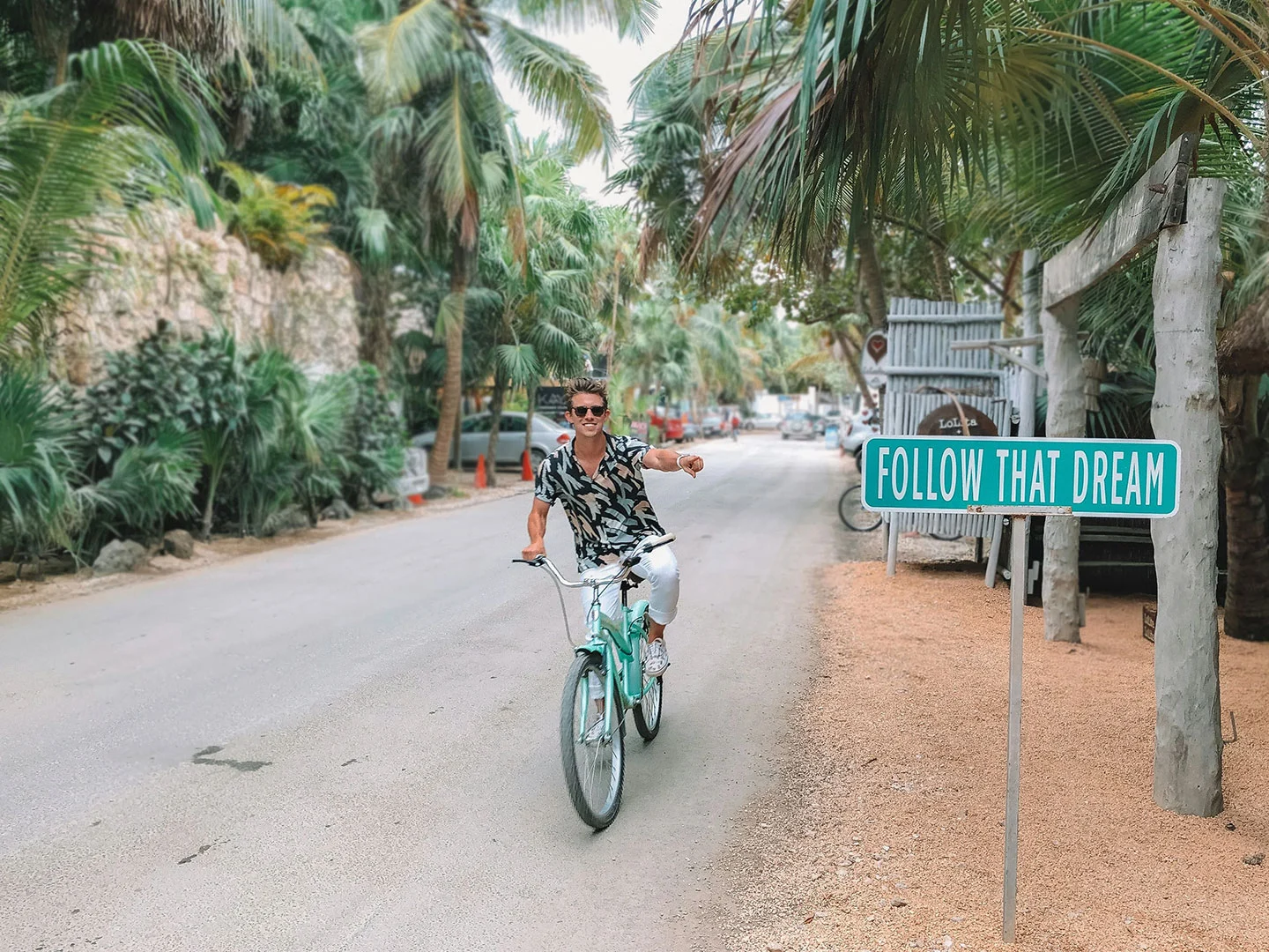 man riding bike and pointing to a sign that says follow that dream